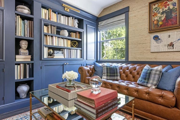Kristine Bishop Design Dark Blue Book Shelf Cabinets Brown Leather Couch Tartan Pillows Red Persian Rug Glass Coffee Table Textured Biege Wall Paper