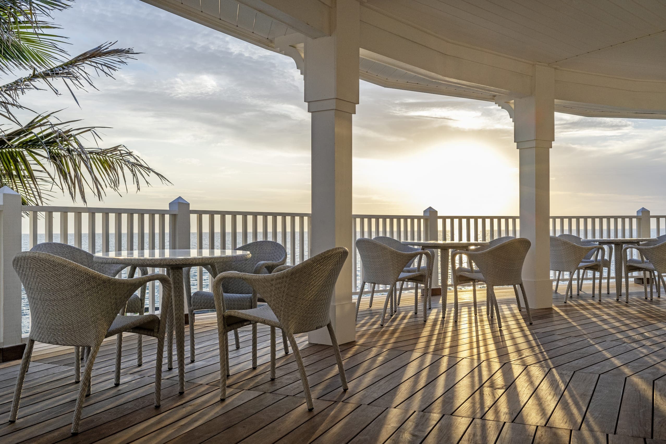 Wicker Chairs And Circular Dining Tables With Sunset Balcony View